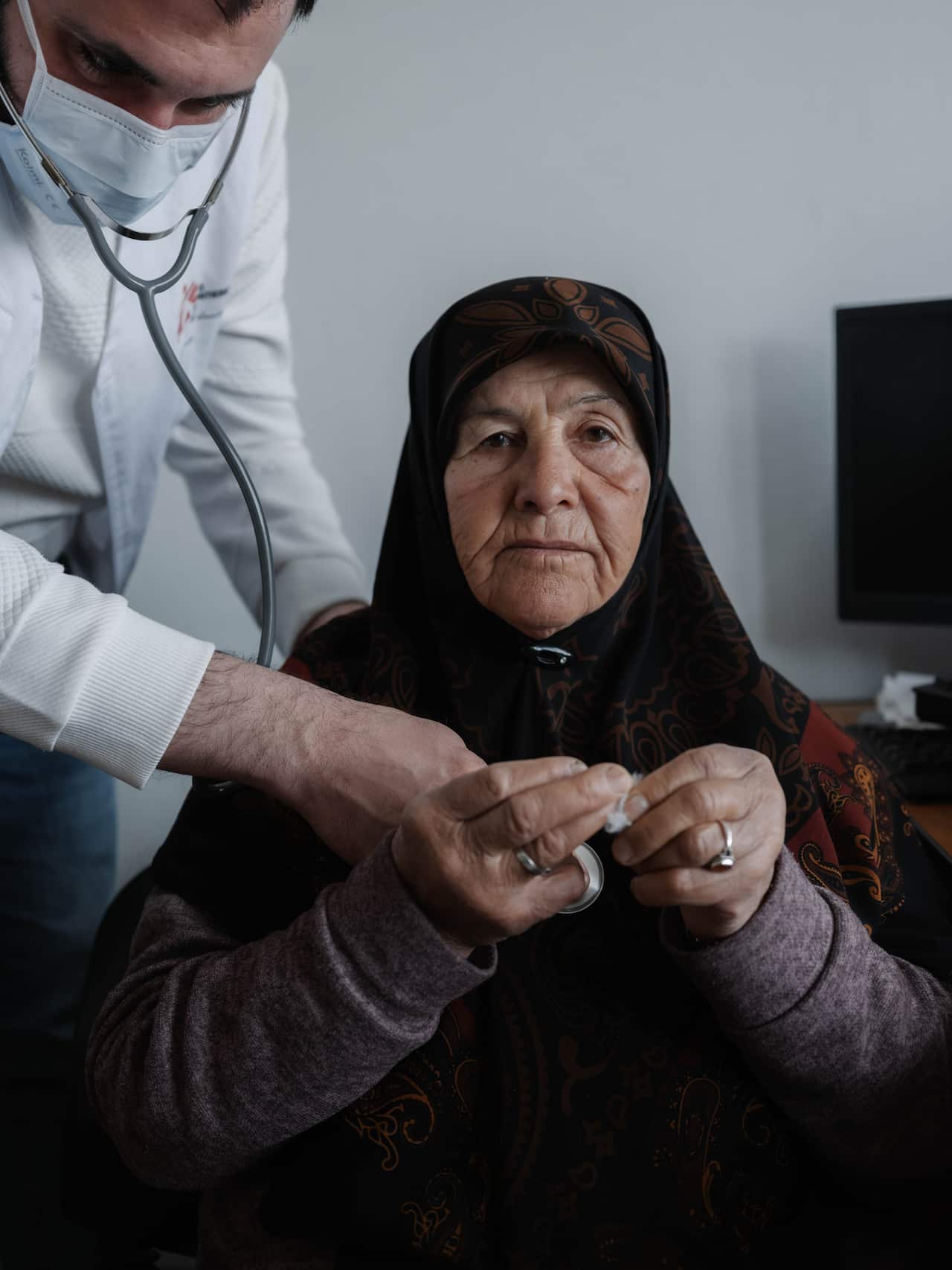 An older woman is having her heart checked with a stethoscope by a doctor in white.