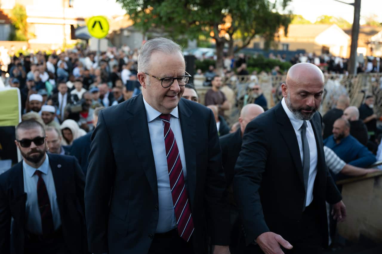 Prime Minister Anthony Albanese walking up stairs, surrounded by a large crowd of people.