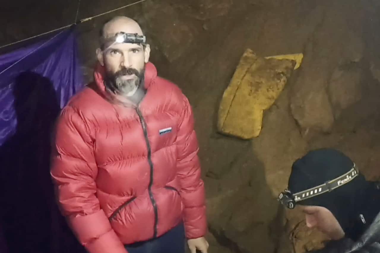 A man in a red puffer jacket with a headtorch, inside a cave