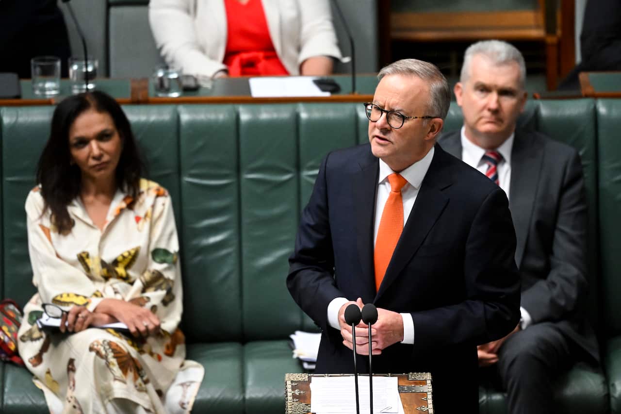 A man in a suit and orange tie speaks at a lecturn. 