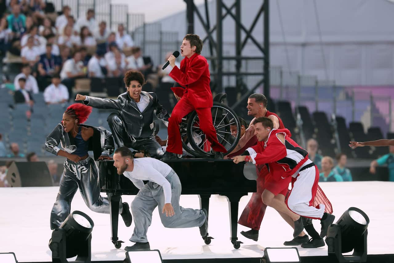 A singer in red performing on top of a piano, surrounded by dancers.