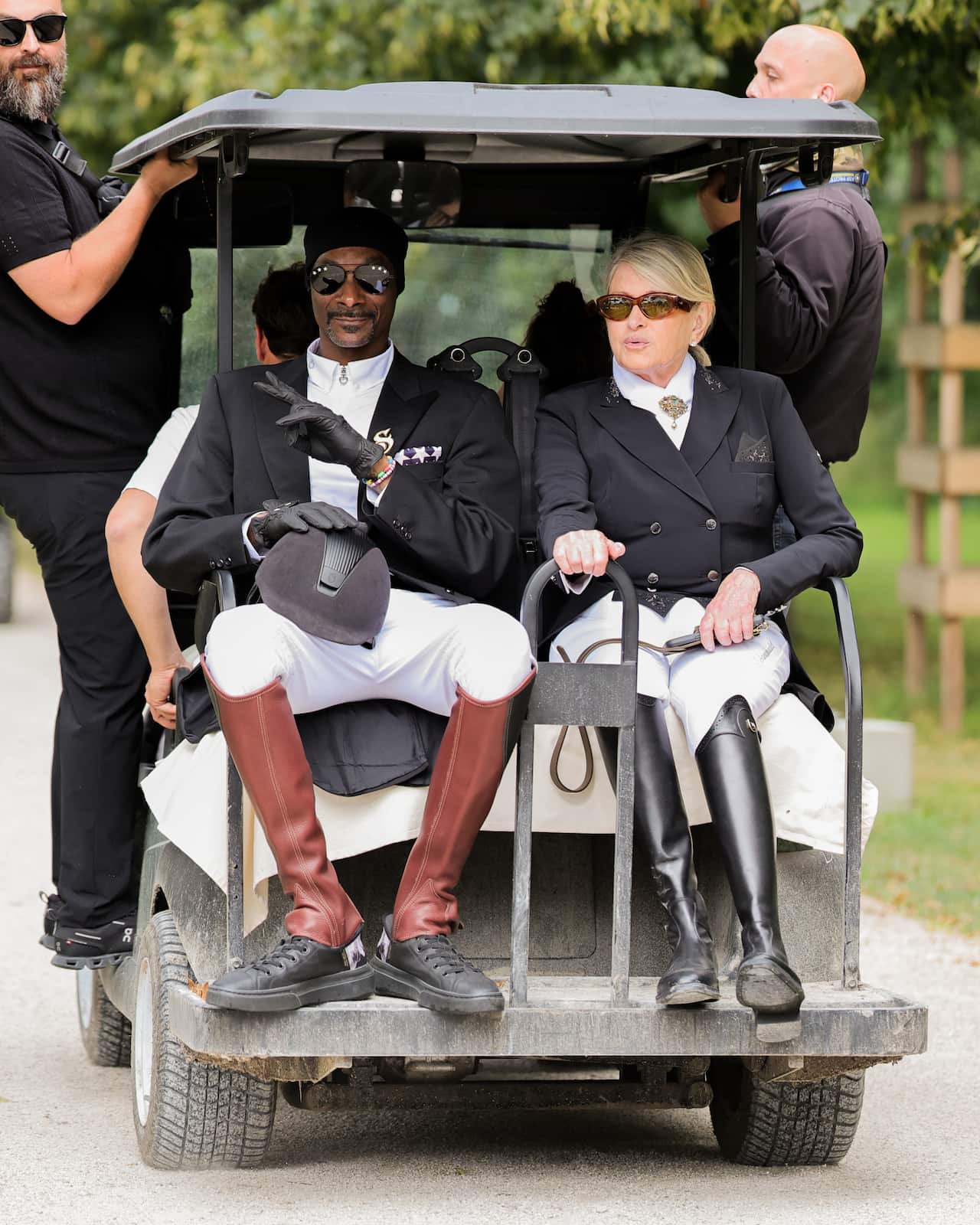 A man and a woman seated on the back of a golf cart.