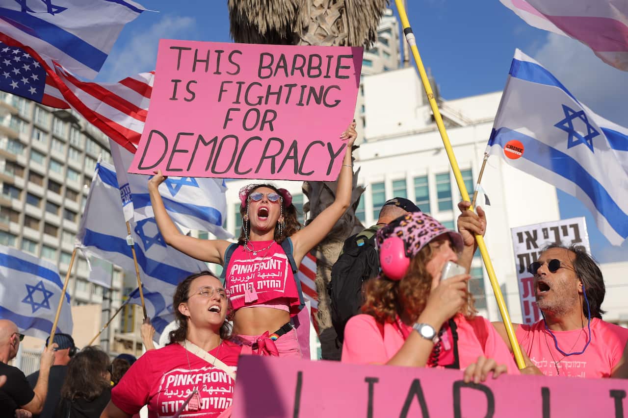 Israeli anti-government protesters hold banners and flags during a protest.