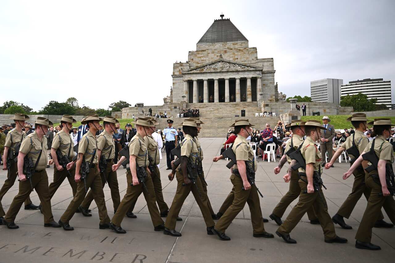 A group of soldiers march as people look on.