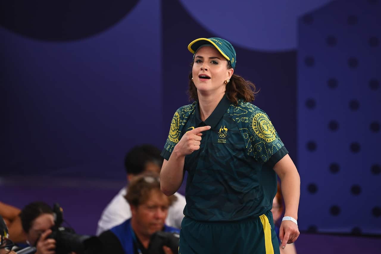 A woman in a green and gold outfit breakdancing. There is a purple background behind her.