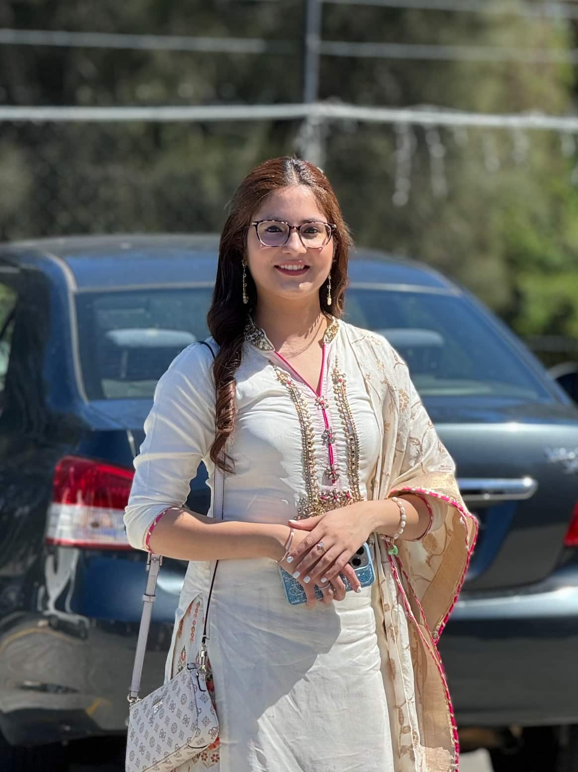 A woman standing in front of a car, smiling.