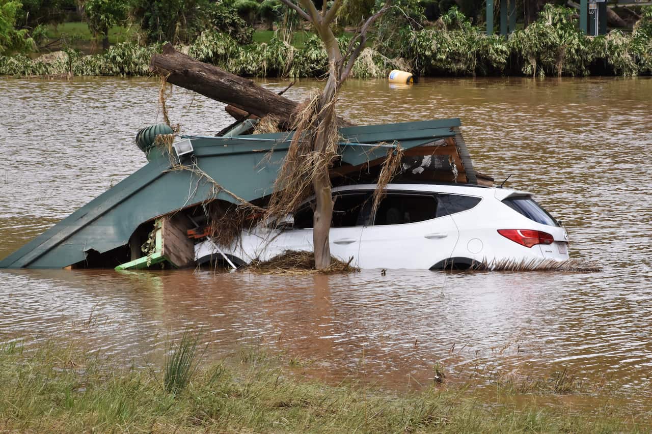 A white car in floodwaters with debris on top of it