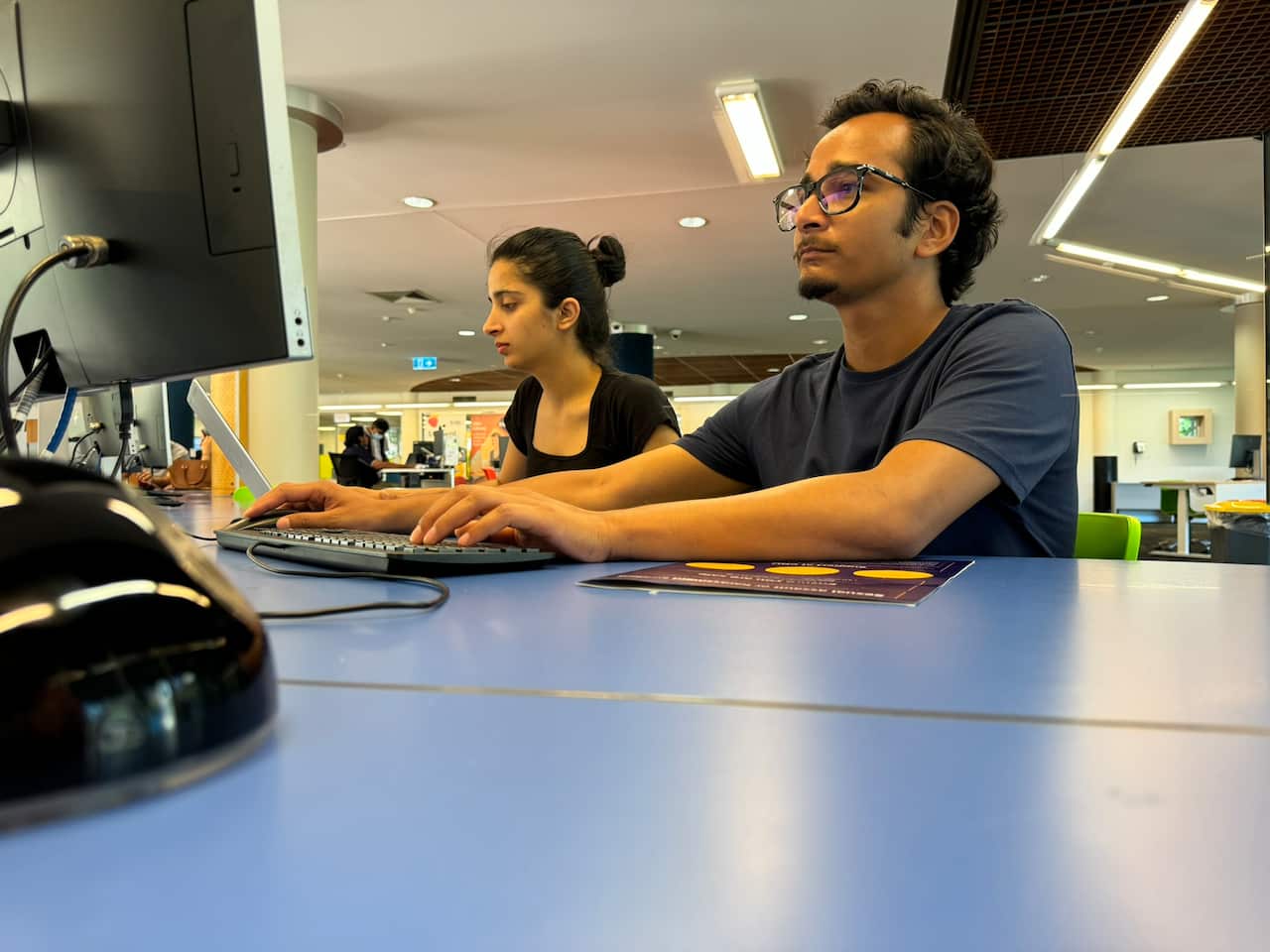 A woman and man sitting at a computer desk in a library.