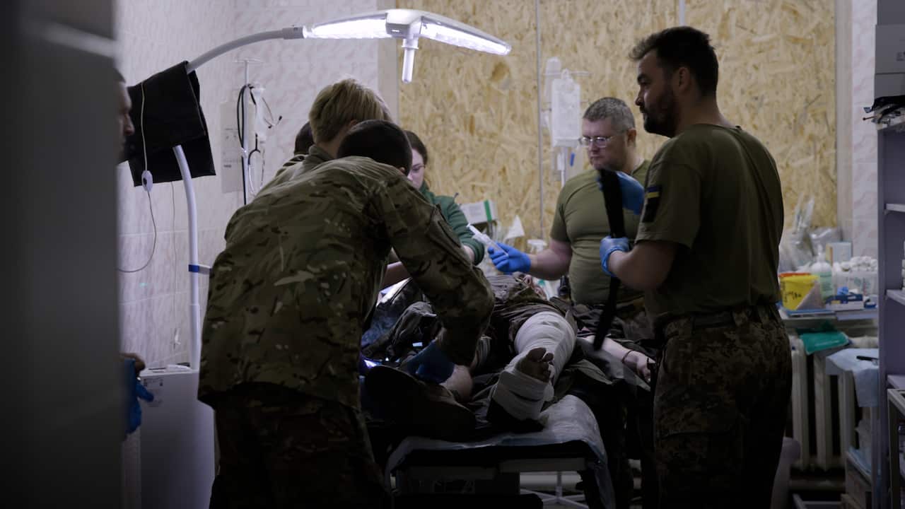 Combats medics in military fatigues treating a wounded soldier on an operating table at a military field hospital 