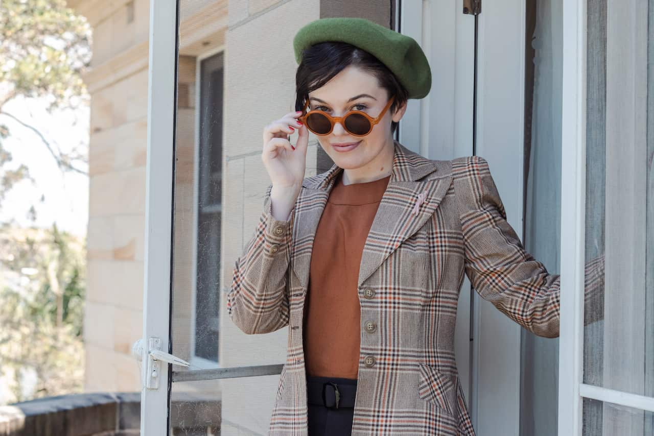 A woman pulls her sunglasses down her nose to look in the camera lens