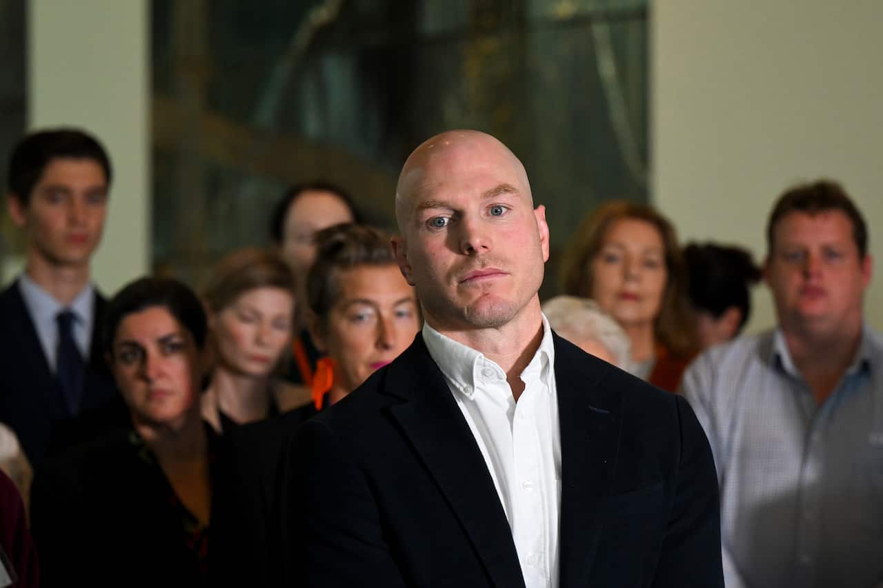 Man in open collared shirt standing in front of a group of people.