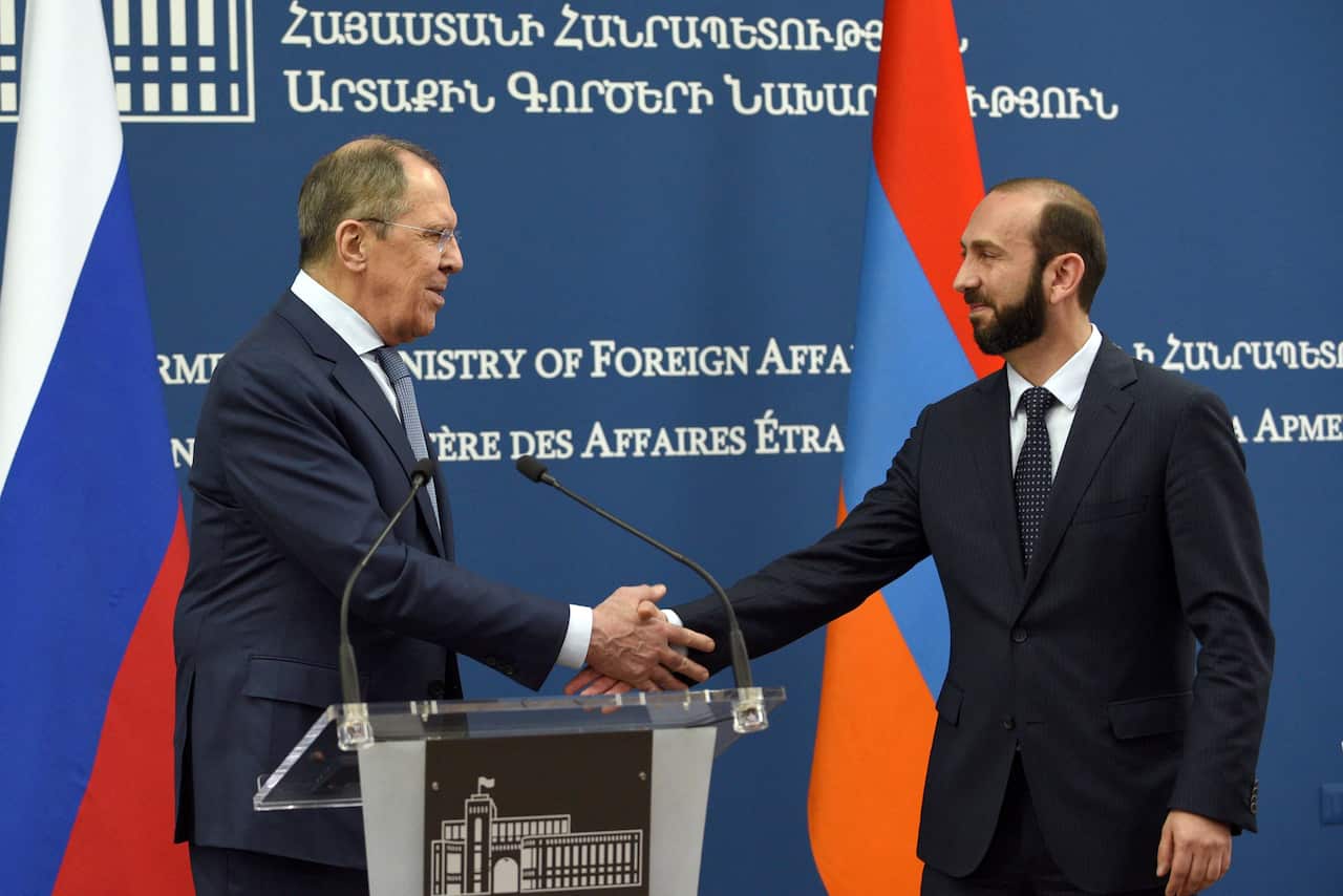 Two men shake hands in front of the Russian and Armenia flags