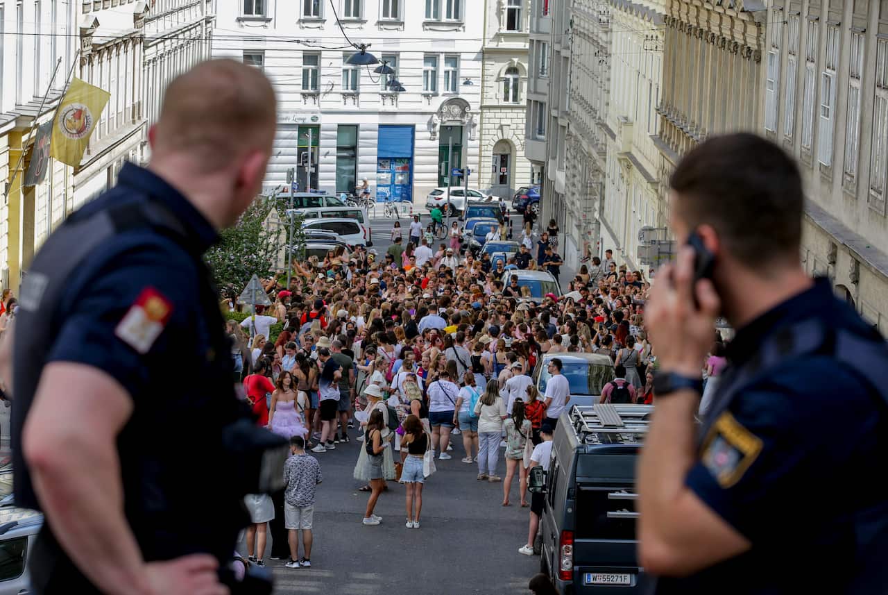 Austrian police officers watch a large group of people gathering in a city centre.