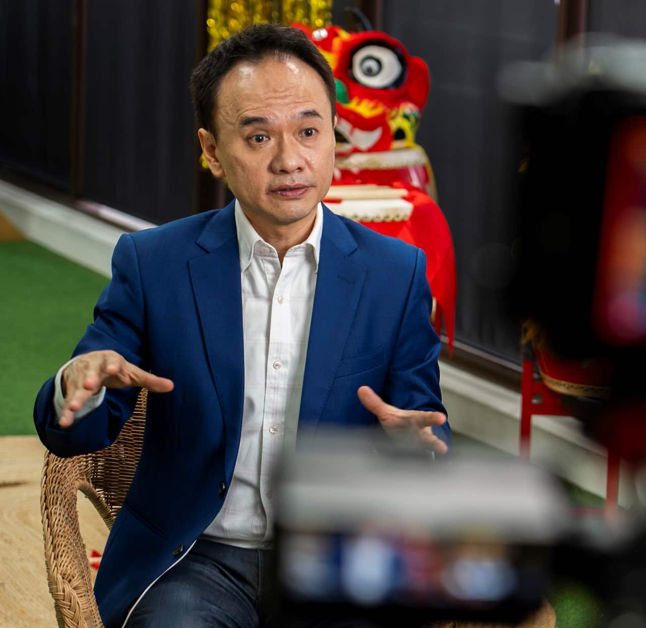 A man in a blue suit jacket sits, speaking to the camera.