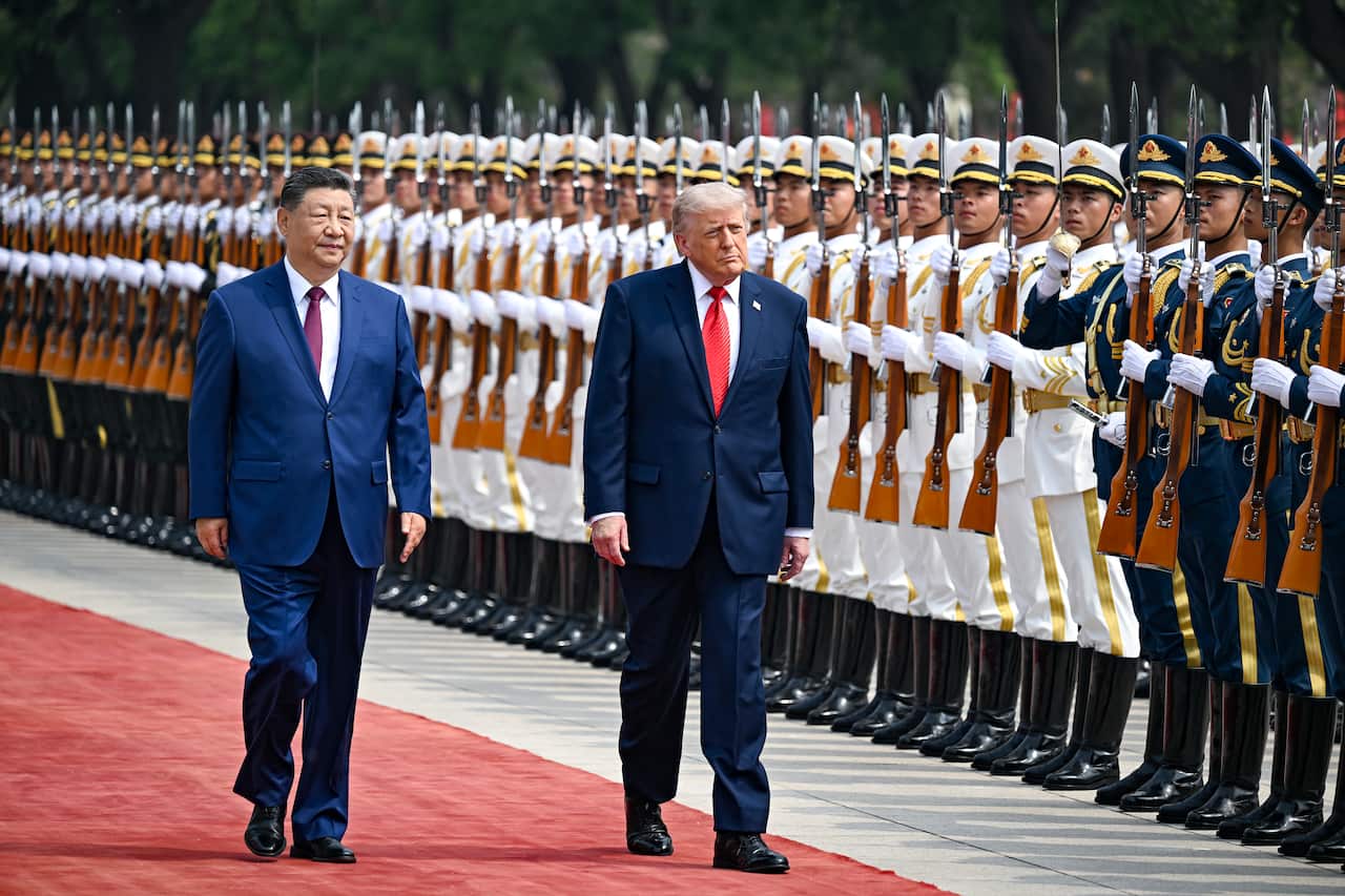 An older white man and an older asian man walking past soldiers in formation 