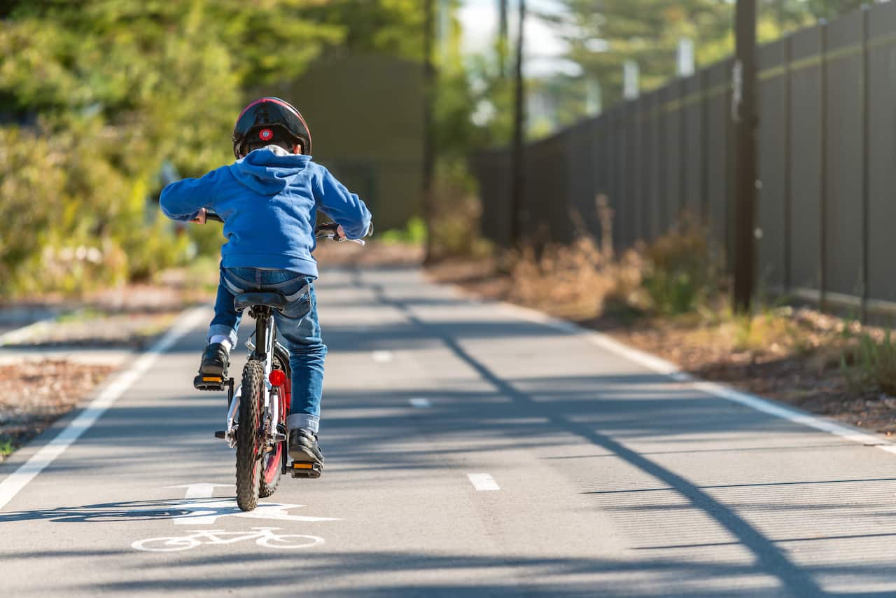 A child in a blue sweater rides a bicycle on a bike lane