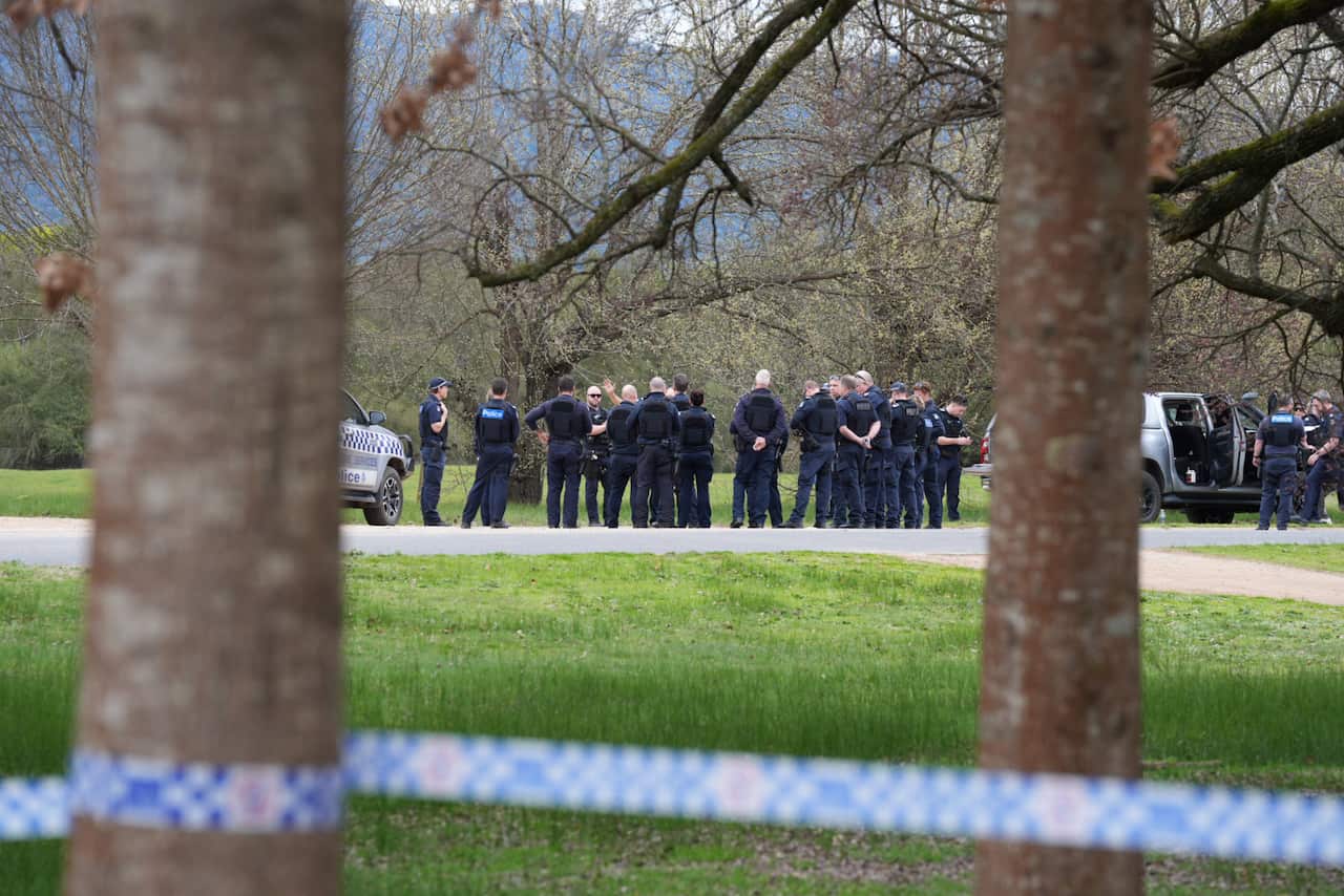 A large group of police standing on a road. Police tape is in front of them.