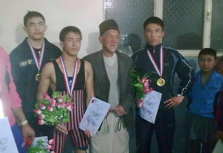 Three men wearing medals and holding flowers stand with another man