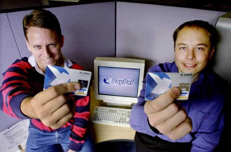 Two men sitting in front of an old computer holding up bank cards