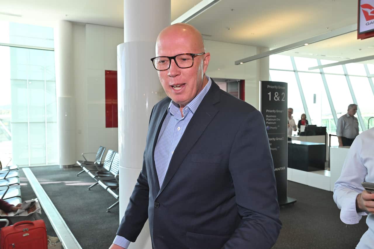 Former Opposition leader Peter Dutton, wearing a suit, tie and glasses, talking to journalists while walking inside and airport.