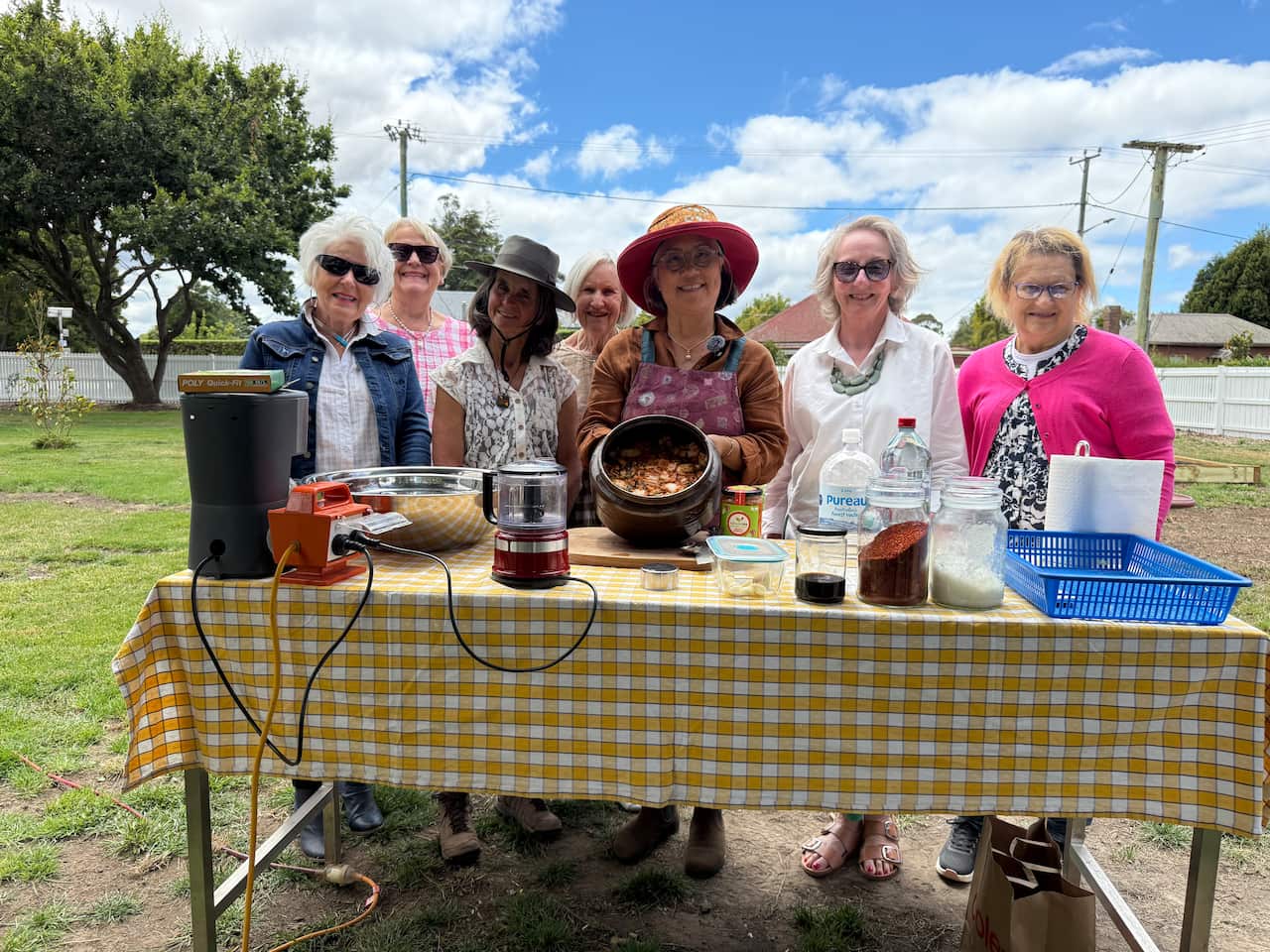 A group of women smiling and holding a container of kimchi over a table