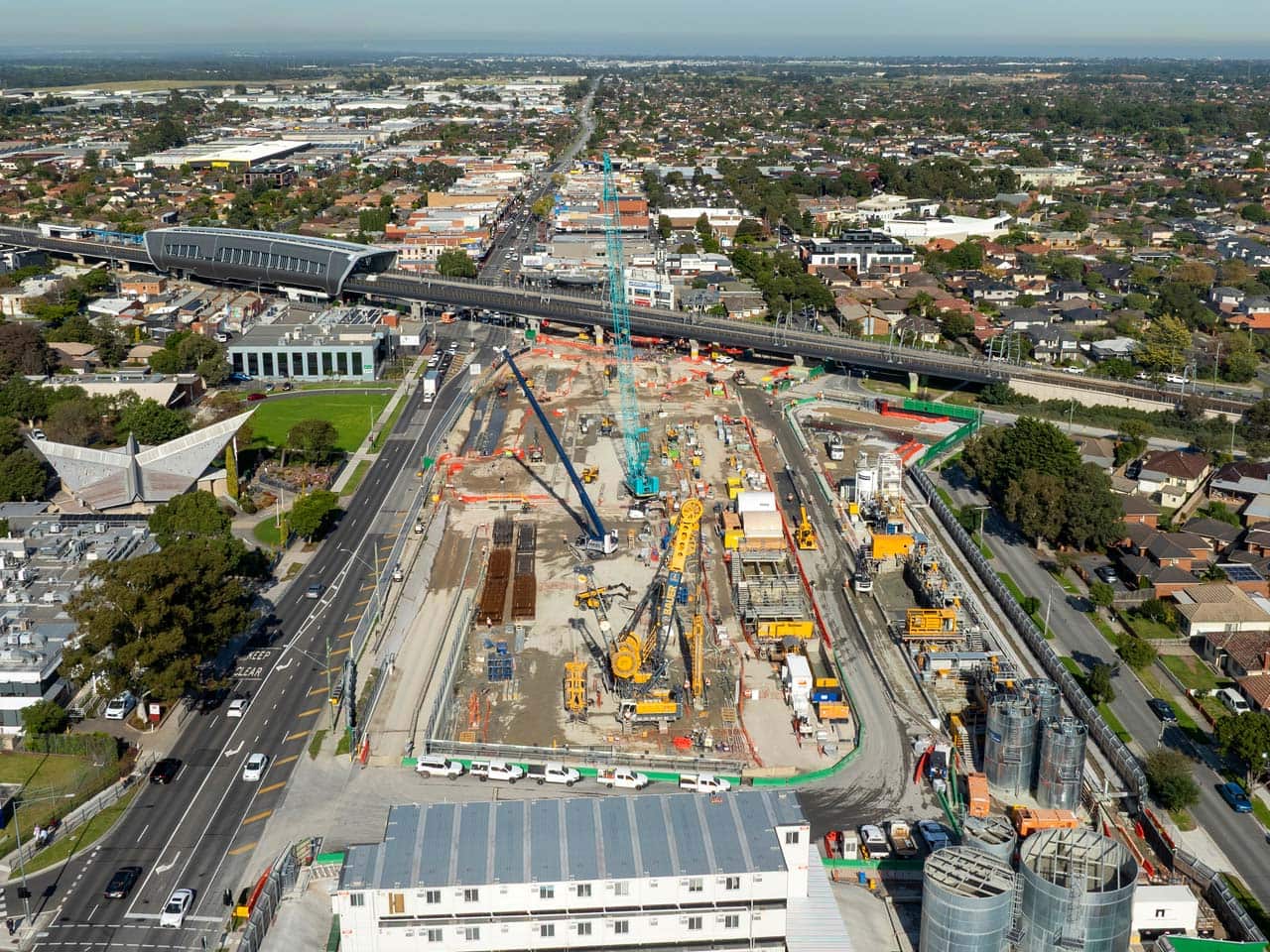 An aerial shot of a construction site showing cranes and other machinery, surrounded by roads and rail line