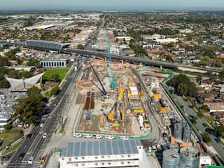 An aerial shot of a construction site showing cranes and other machinery, surrounded by roads and rail line
