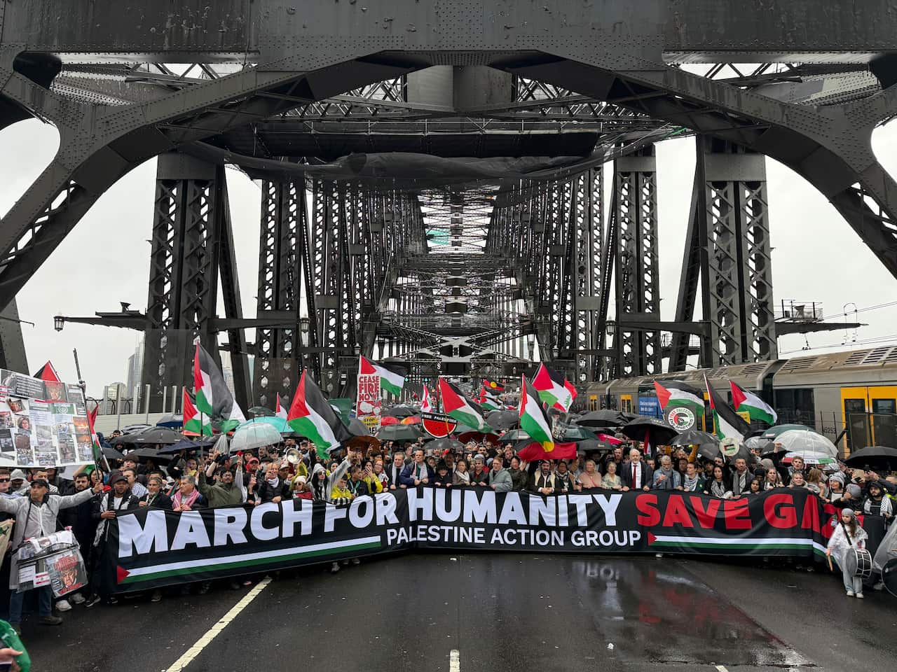 A large group of protesters crosses the Sydney Harbour Bridge carrying a banner reading "March for Humanity. Save Gaza."