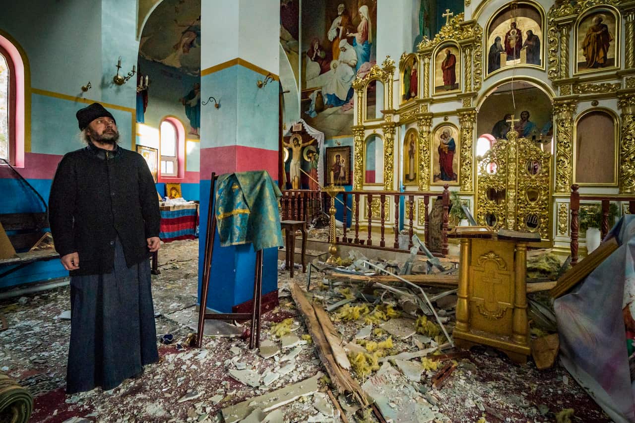 A priest stands inside a destroyed church.