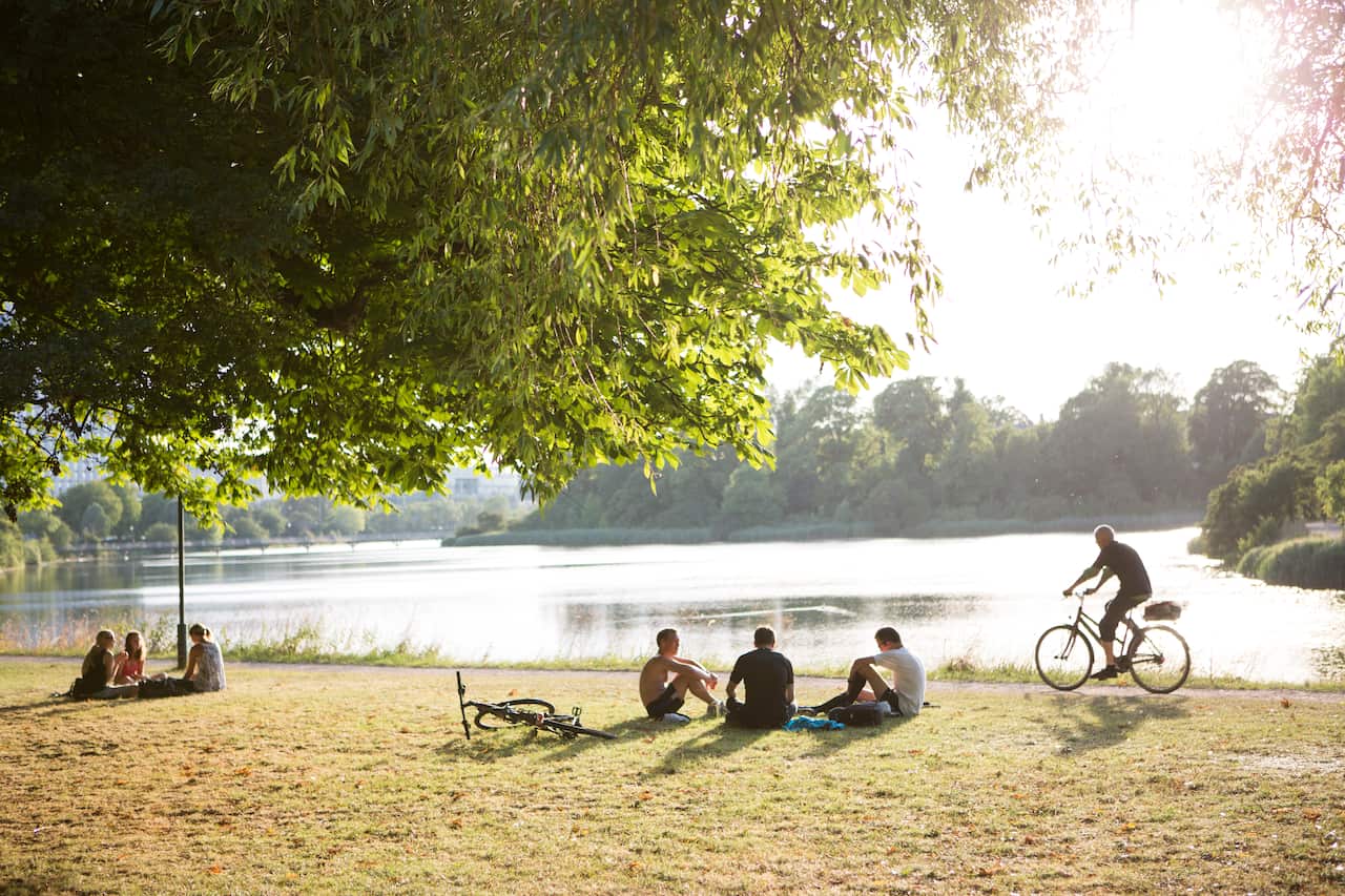 People relaxing in a park next to a lake at sunset
