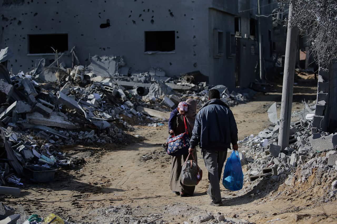 People walking past the rubble of destroyed houses.