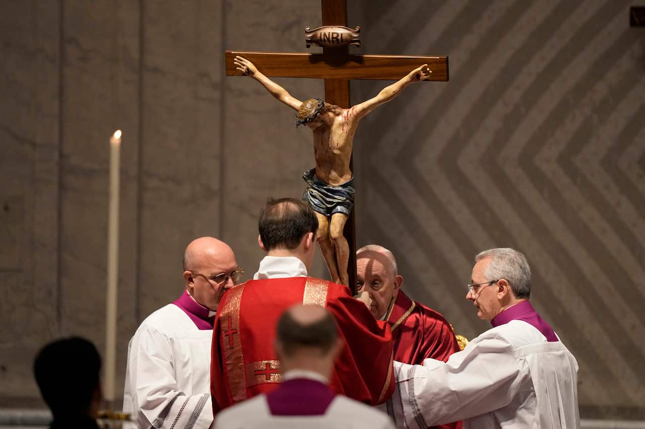 Pope Francis and priests hold onto an ornament of Jesus on the cross. 