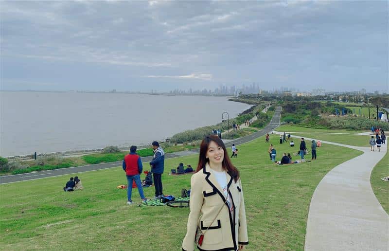 A woman's standing on a grass embankment by water.