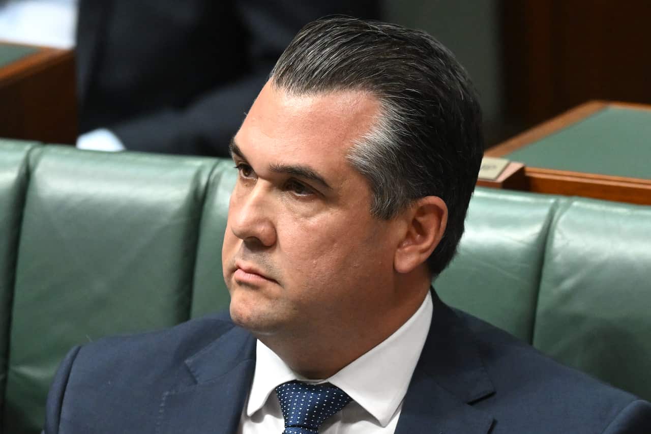 A close up photo of a man in a suit sitting on a green couch in parliament.