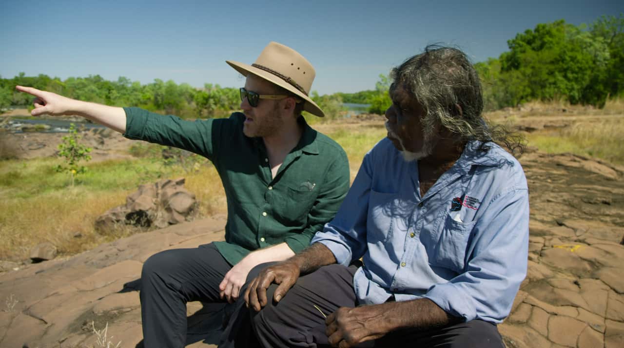 Two men sit down together on a rock face, on Miriwoong Country. 
