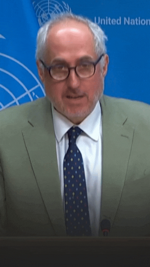 A man in a suit is speaking in front of a blue background.