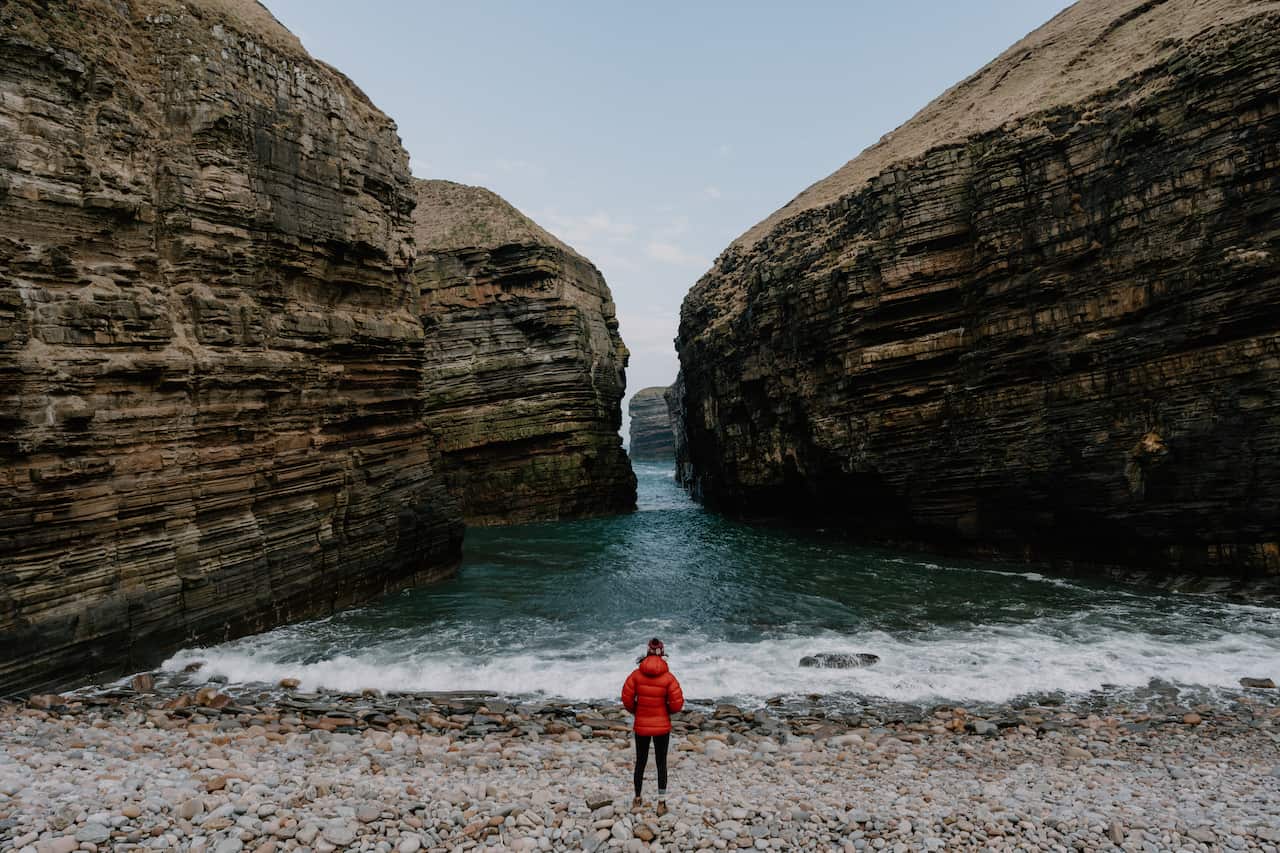 Young woman walks down rocky beach to water's edge