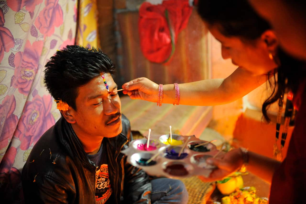 A girl applies seven layers of colorful vermilion powder (tika) on her brothers' forehead during Bhai Tika. 