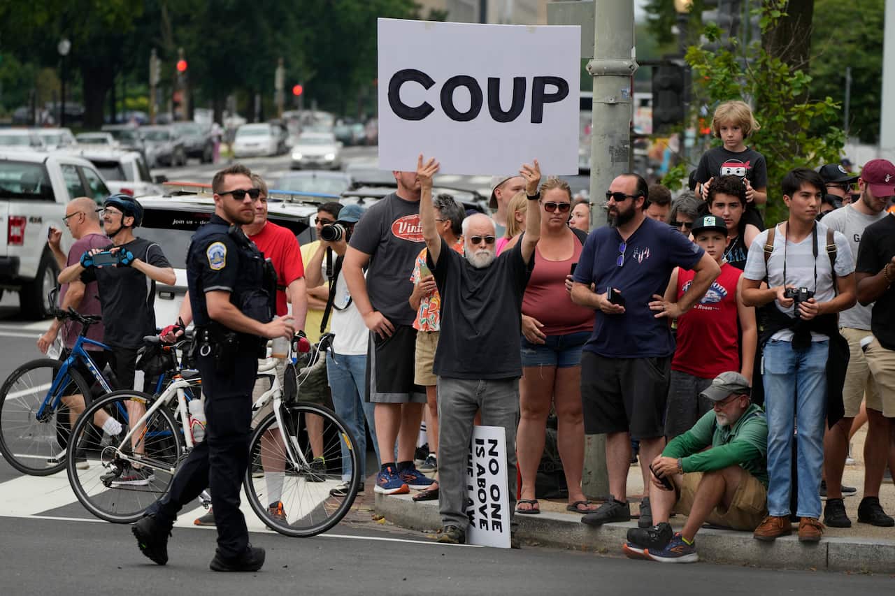 Trump supporters standing on a corner carrying a sign that says "coup"