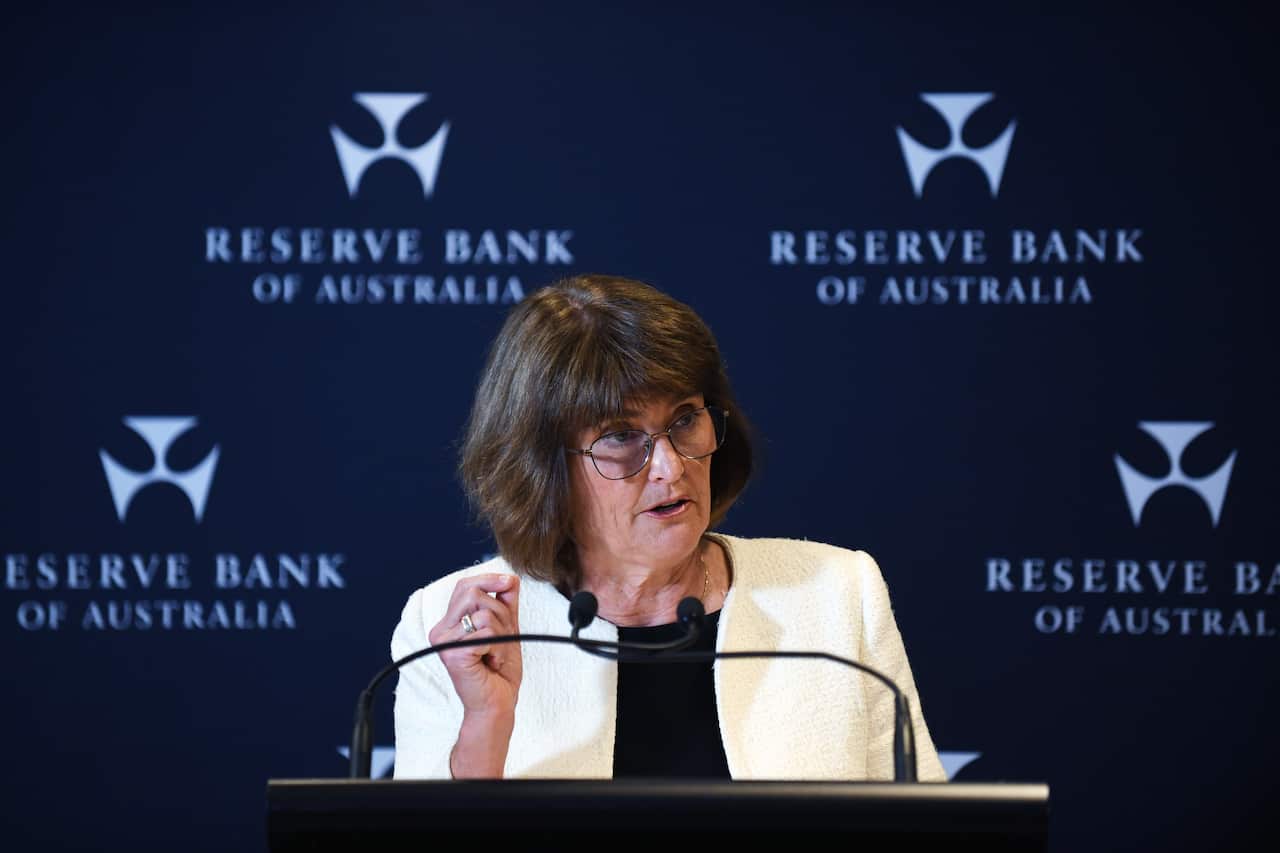 A woman in a white blazer speaks at a podium, with several Reserve Bank of Australia logos displayed on a blue background.