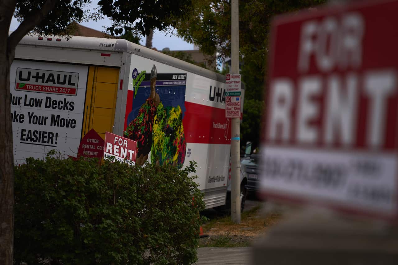 A truck with a logo that reads "U-Haul" is parked next to a "For Rent" sign.