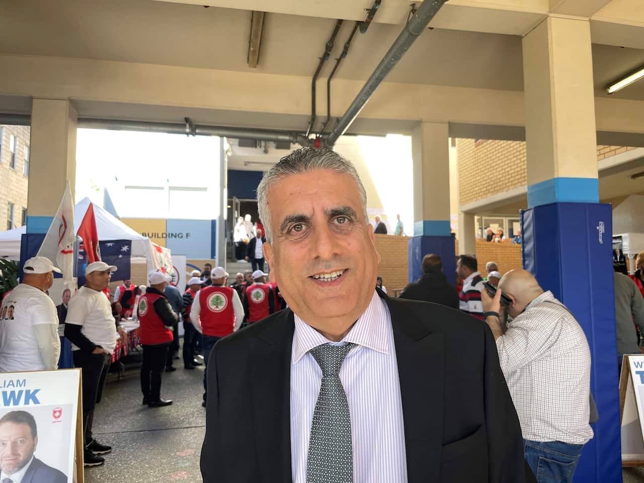 Elie stands in the centre in a suit, smiling in front of voters and volunteers at the Lebanon election.