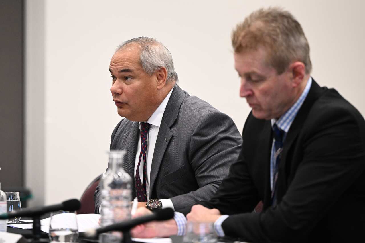 Two men sitting at a table during a federal government inquiry.