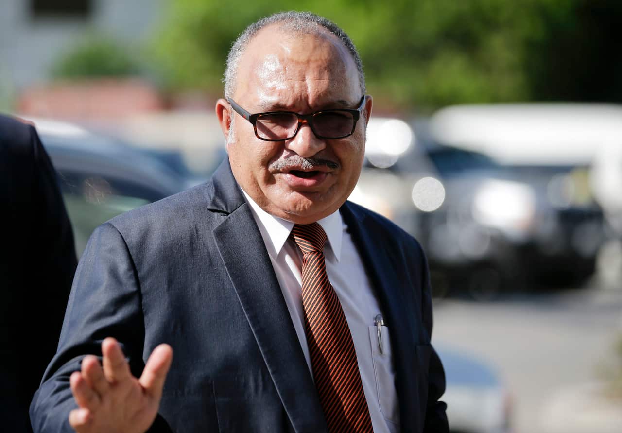 Peter O'Neill in a suit holding his right hand up 