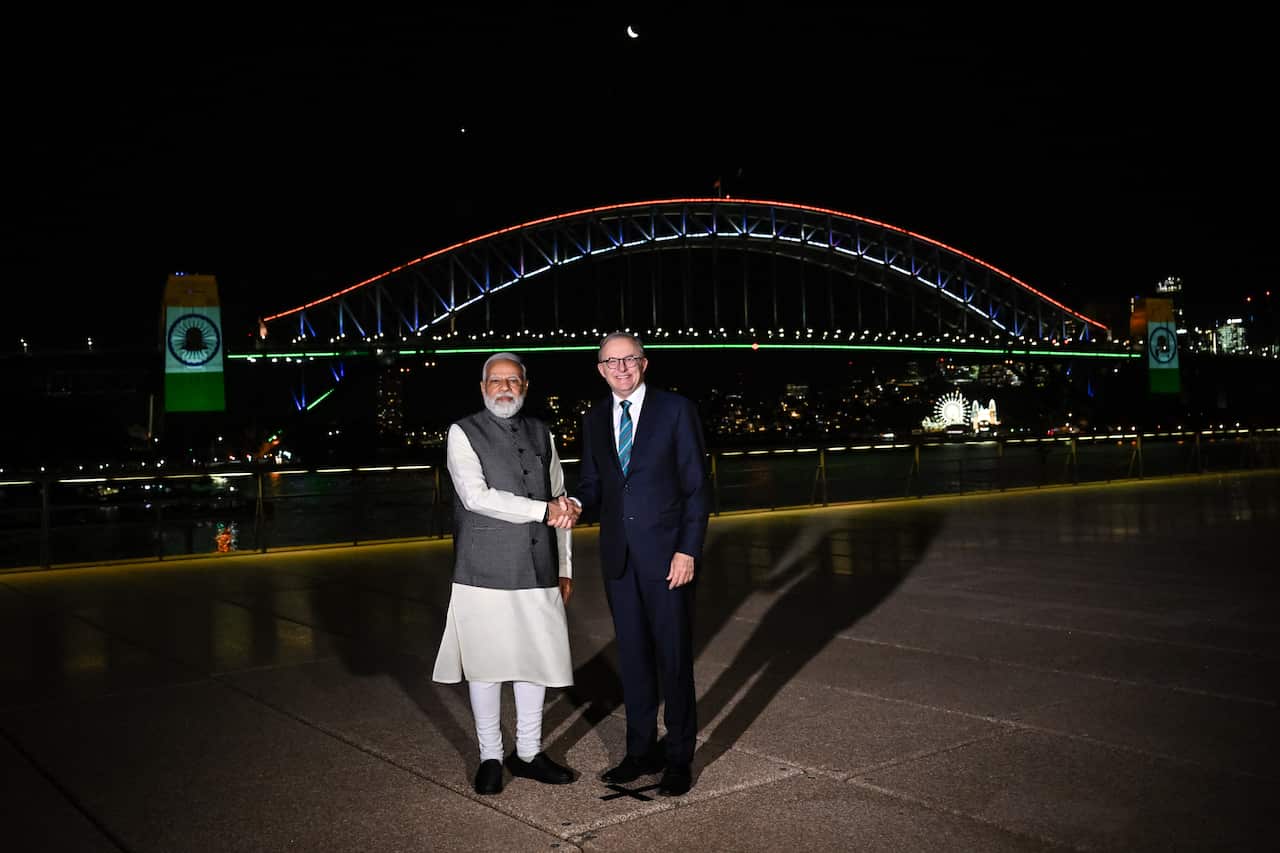 Two men seen shaking hands in front of a Sydney Harbour Bridge lit up in Indian national colours at night.