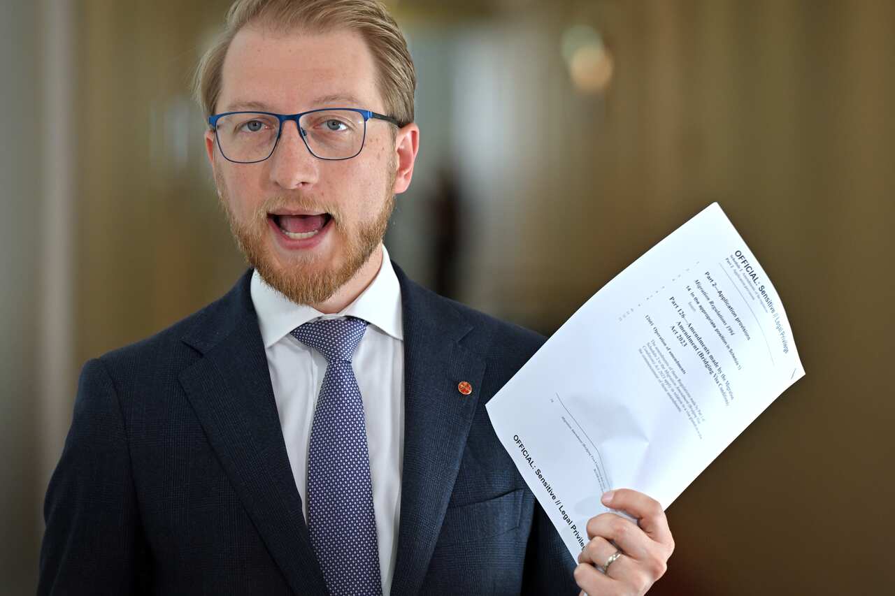 A picture of a man with combed back hair in a suit holding a sheet of paper. 