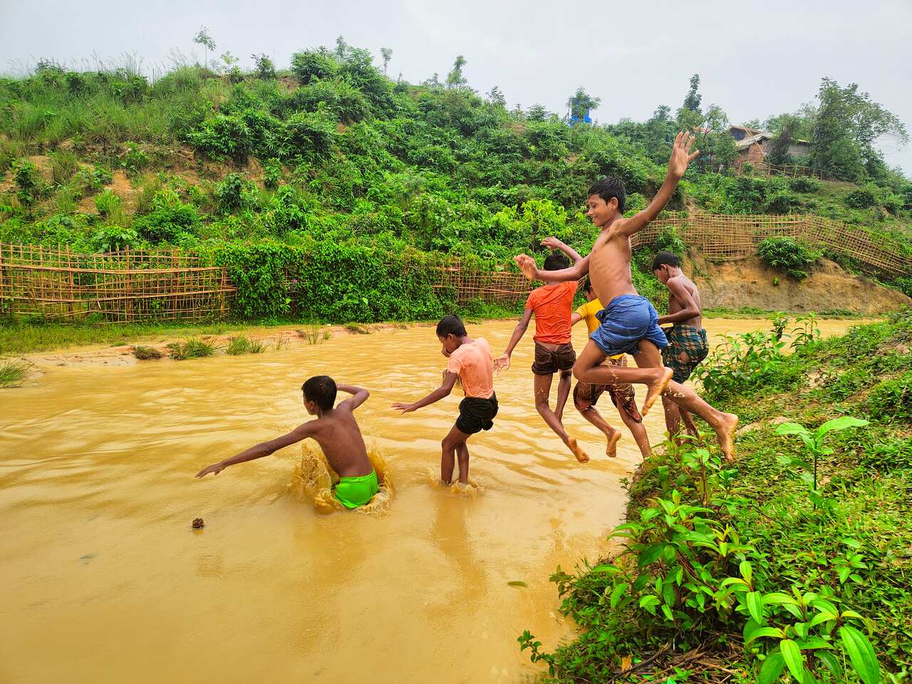 Six young boys jumping into a muddy river.