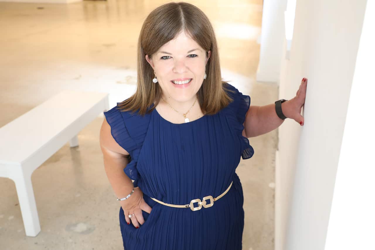A smiling woman of short stature wears a blue dress.