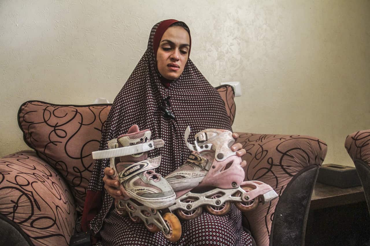 A woman in red hijab with white dots sitting on a couch. She looks down at pink rollerblades on her lap.
