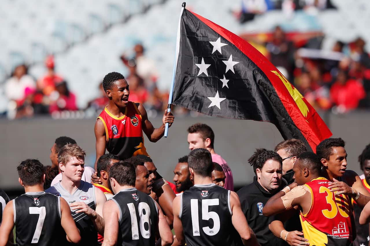 Hewago Oea on the shoulders of a teammate and holding a Papua New Guinea flag after a game of Aussie rule